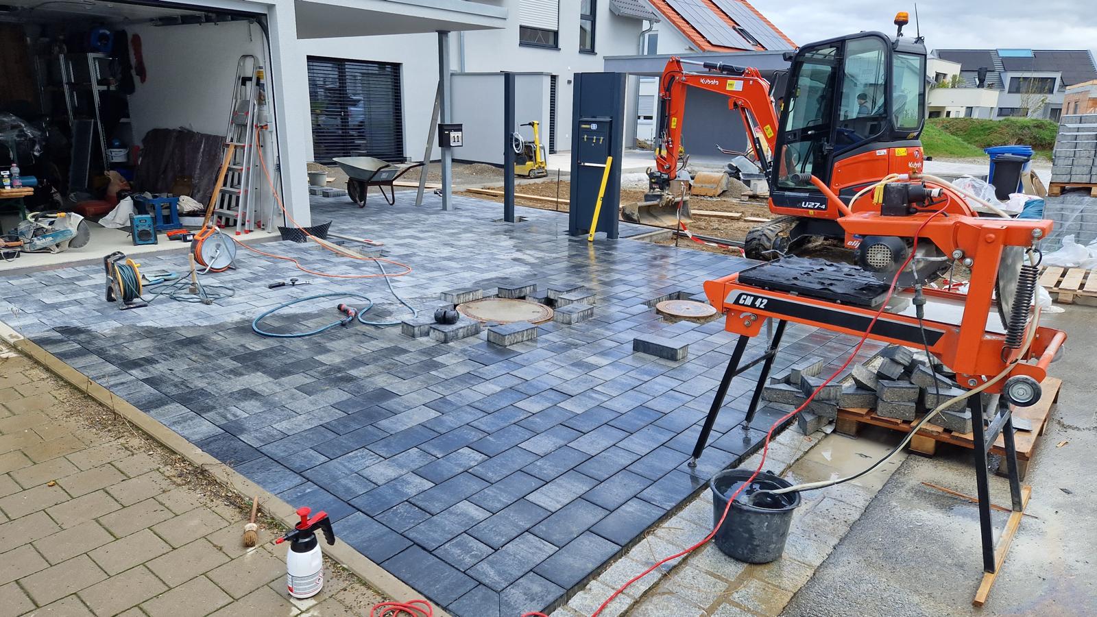 Baustelle mit Minibagger, Steinsäge und teilweise verlegtem Pflaster